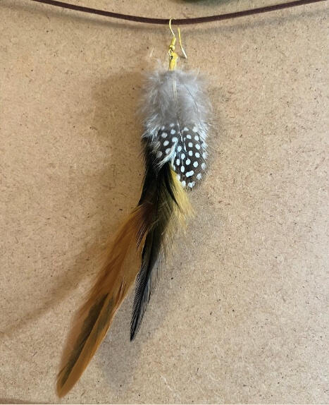 Pendiente artesanal Bruma Dorada con plumas grises, moteadas y tonos dorados y negros en composición natural